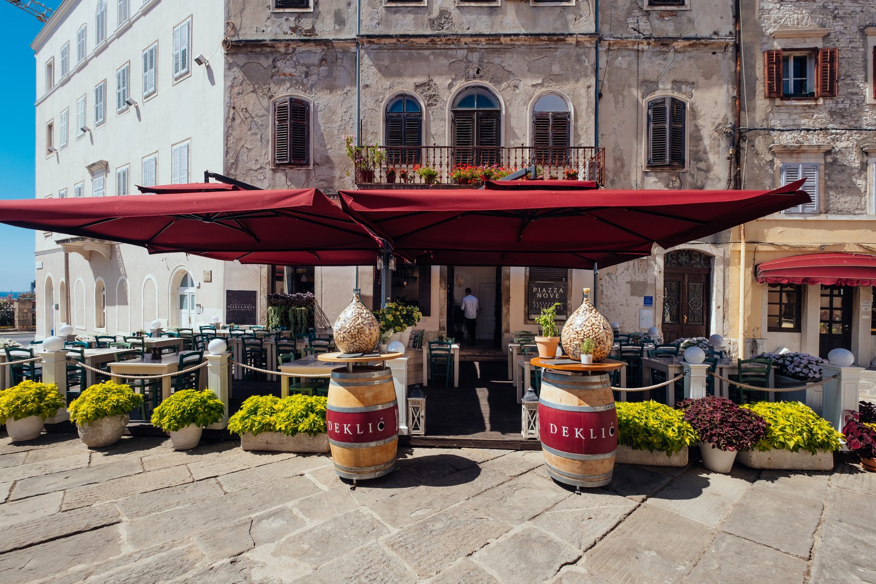 Restaurant Piazza Nove on Kapitolinski trg in Pula — terrace with dark-red parasols against old stone facades
